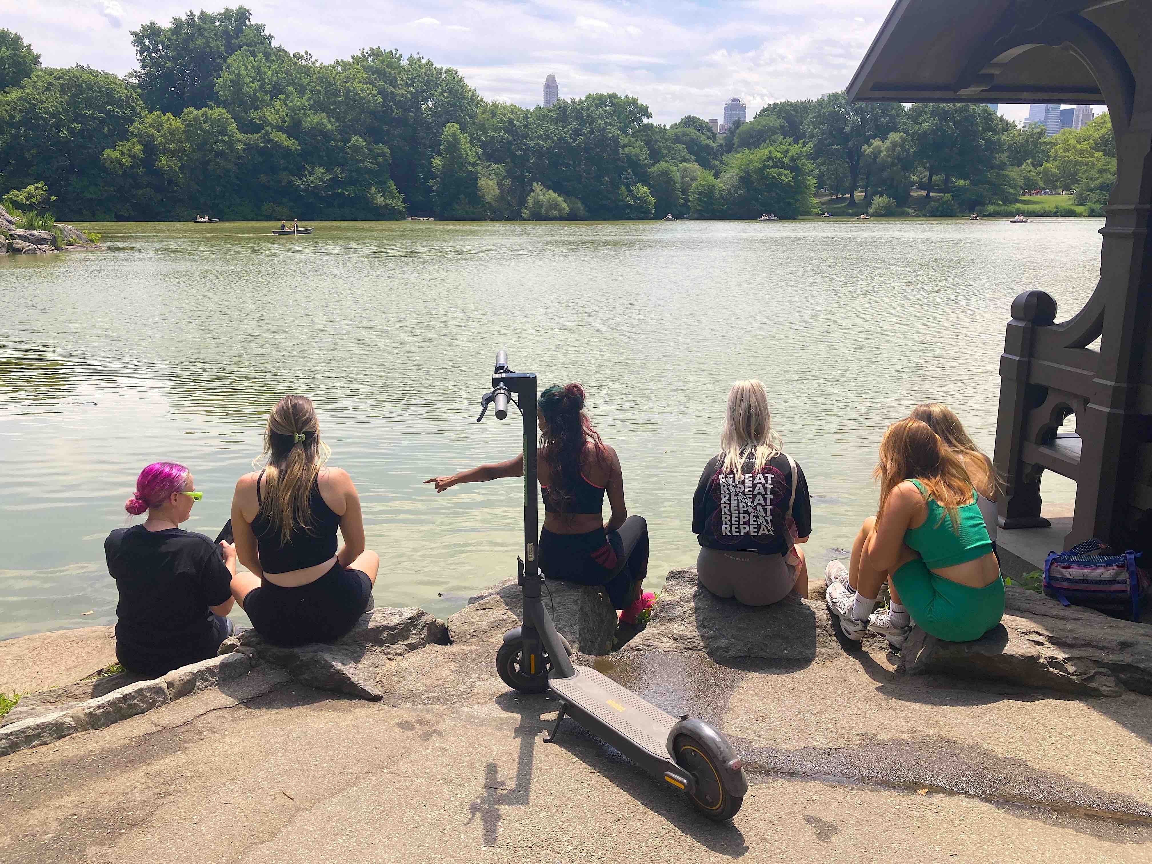 Friends resting by the Lake in Central Park, with the skyline across the water